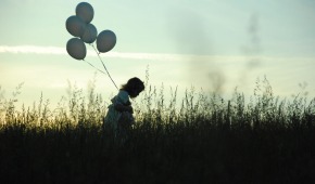 En tjej går med ballonger över en äng